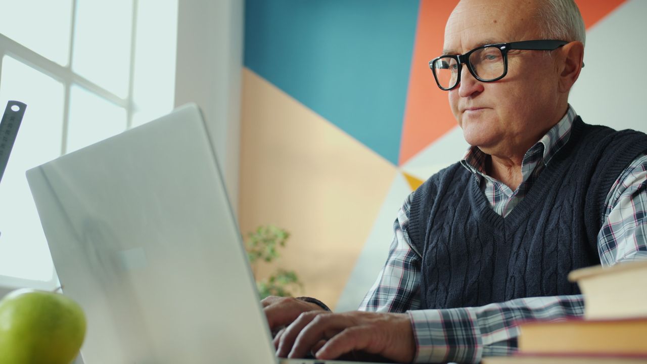 Elderly man focused on his laptop in a stylish, colorful office environment.